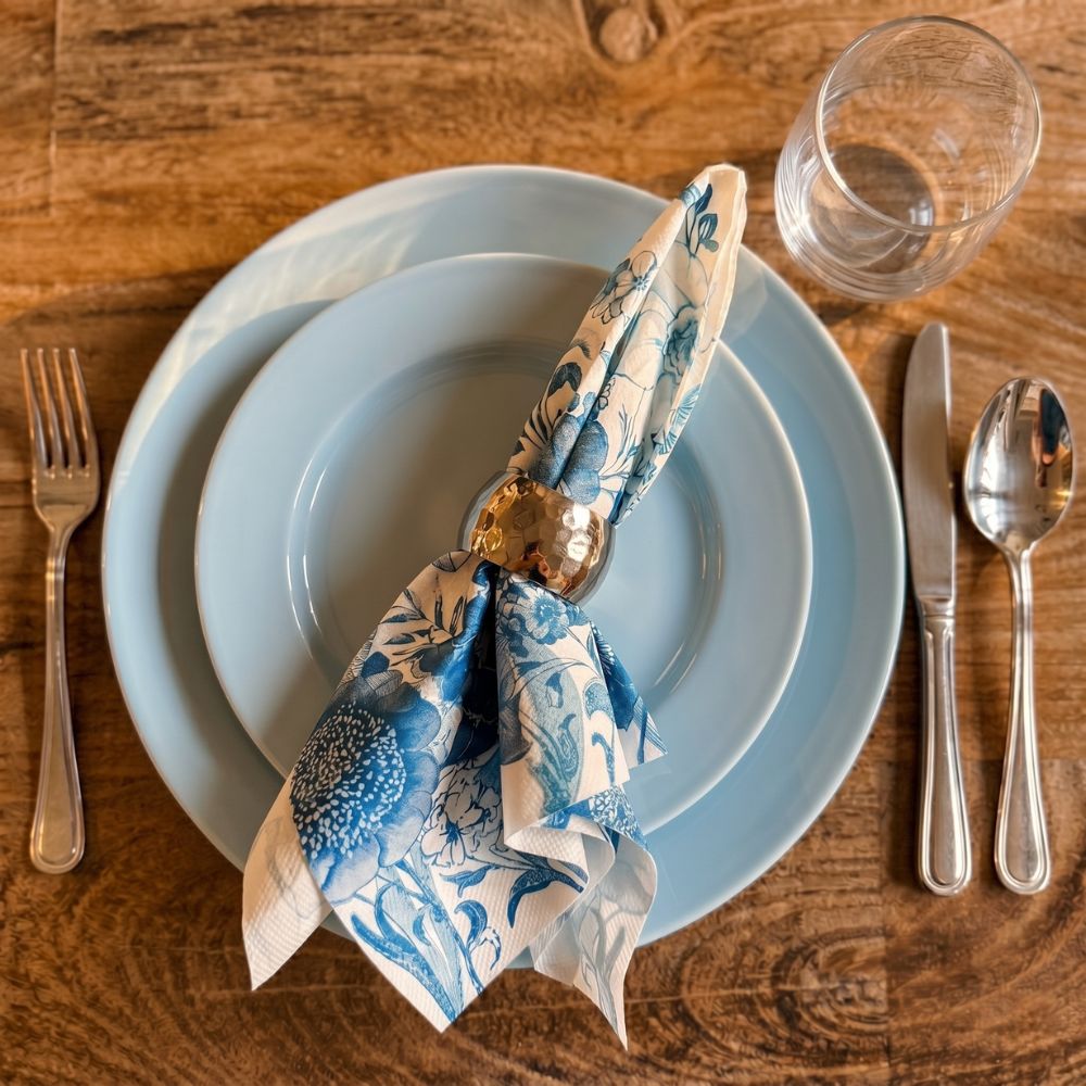 Dinner setting with blue plates, silverware, and a floral napkin on a wooden table.