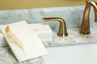 Image of Gold Feather guest towels on a marbled bathroom sink with a gold faucet and handles.