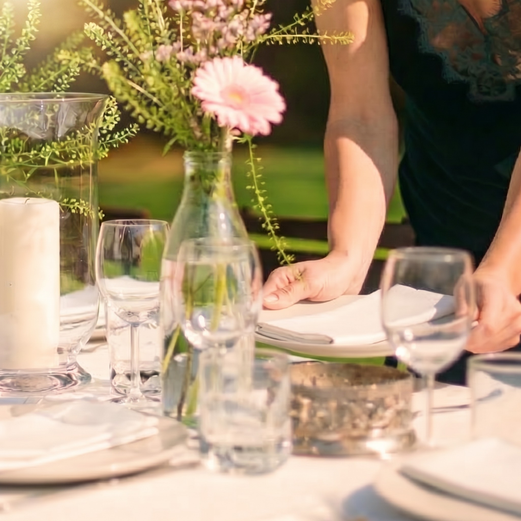 Dining table setting with flowers, glasses, and a person in a blurred background