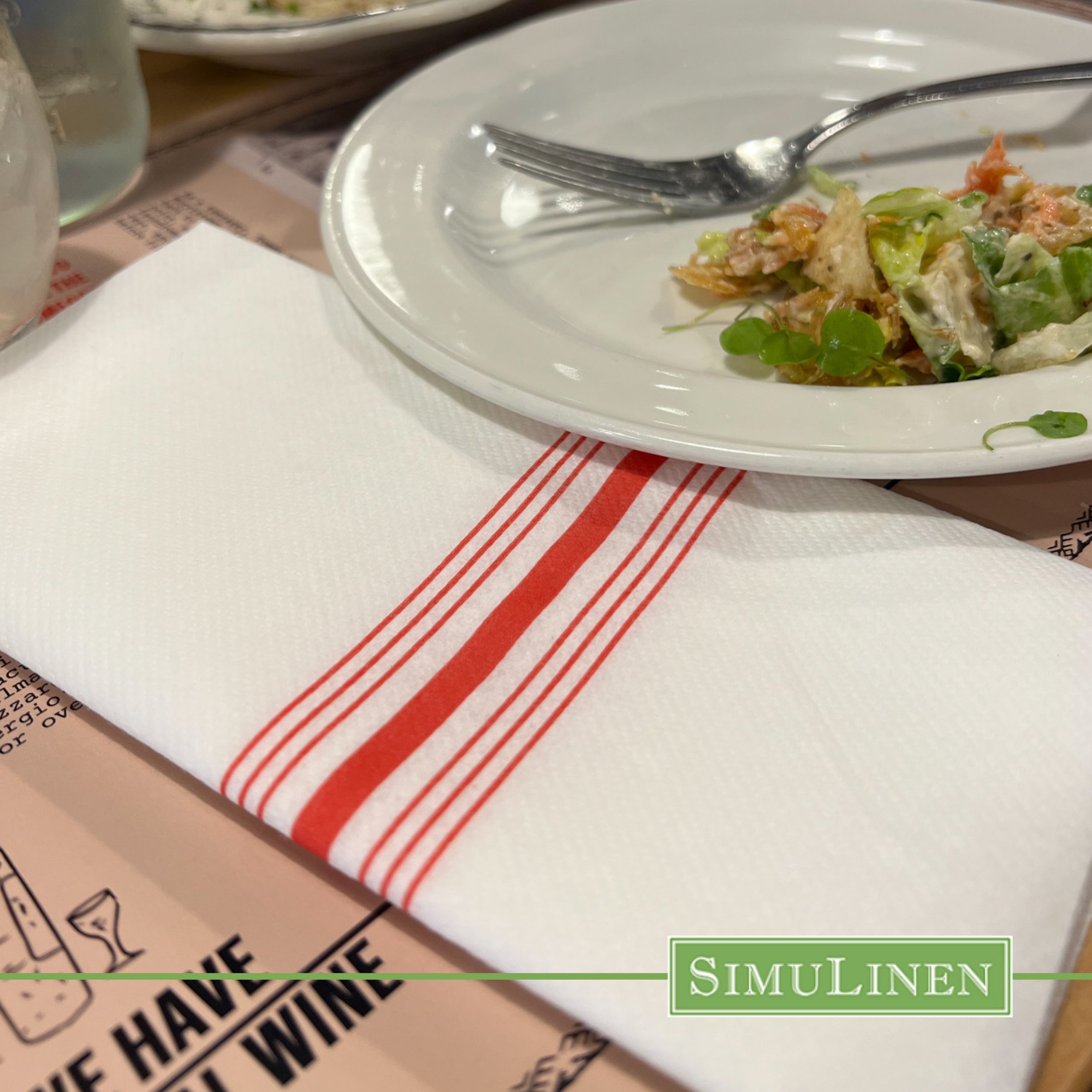 Red bistro stripe SimuLinen dinner napkin on restaurant table with half eaten plate of salad
