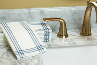 Image of Blue Plaid guest towels on a marbled bathroom sink with a gold faucet and gold handles.