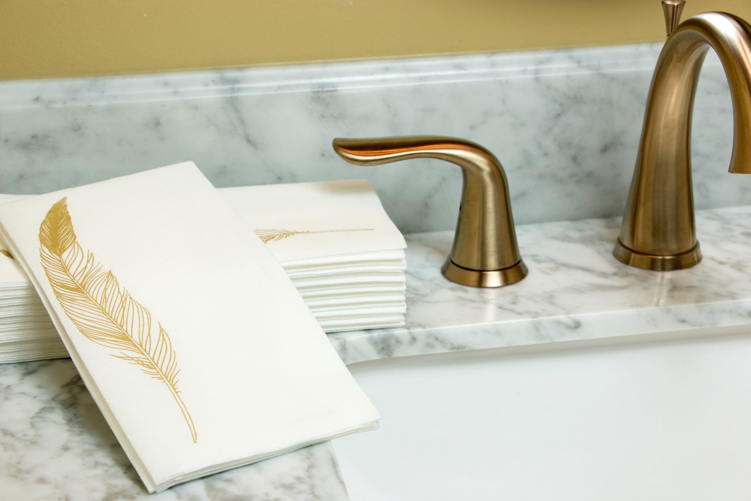 Image of Gold Feather guest towels on a marbled bathroom sink with a gold faucet and handles.